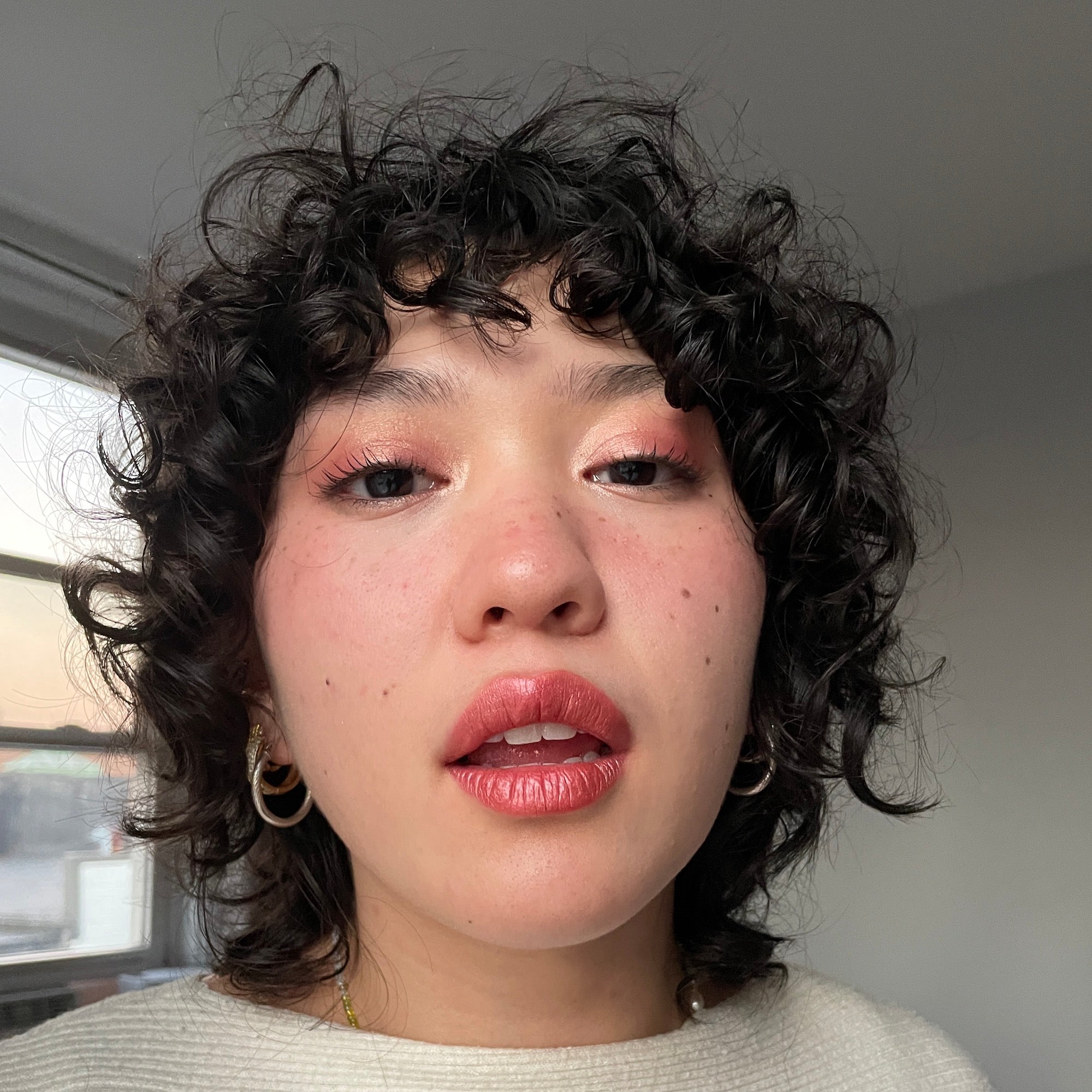 Person with curly hair and pink eyeshadow and lipstick indoors