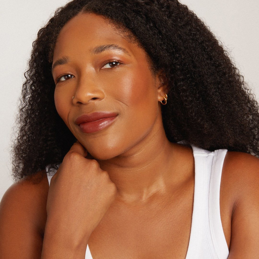 Woman with curly hair wearing makeup against a plain background