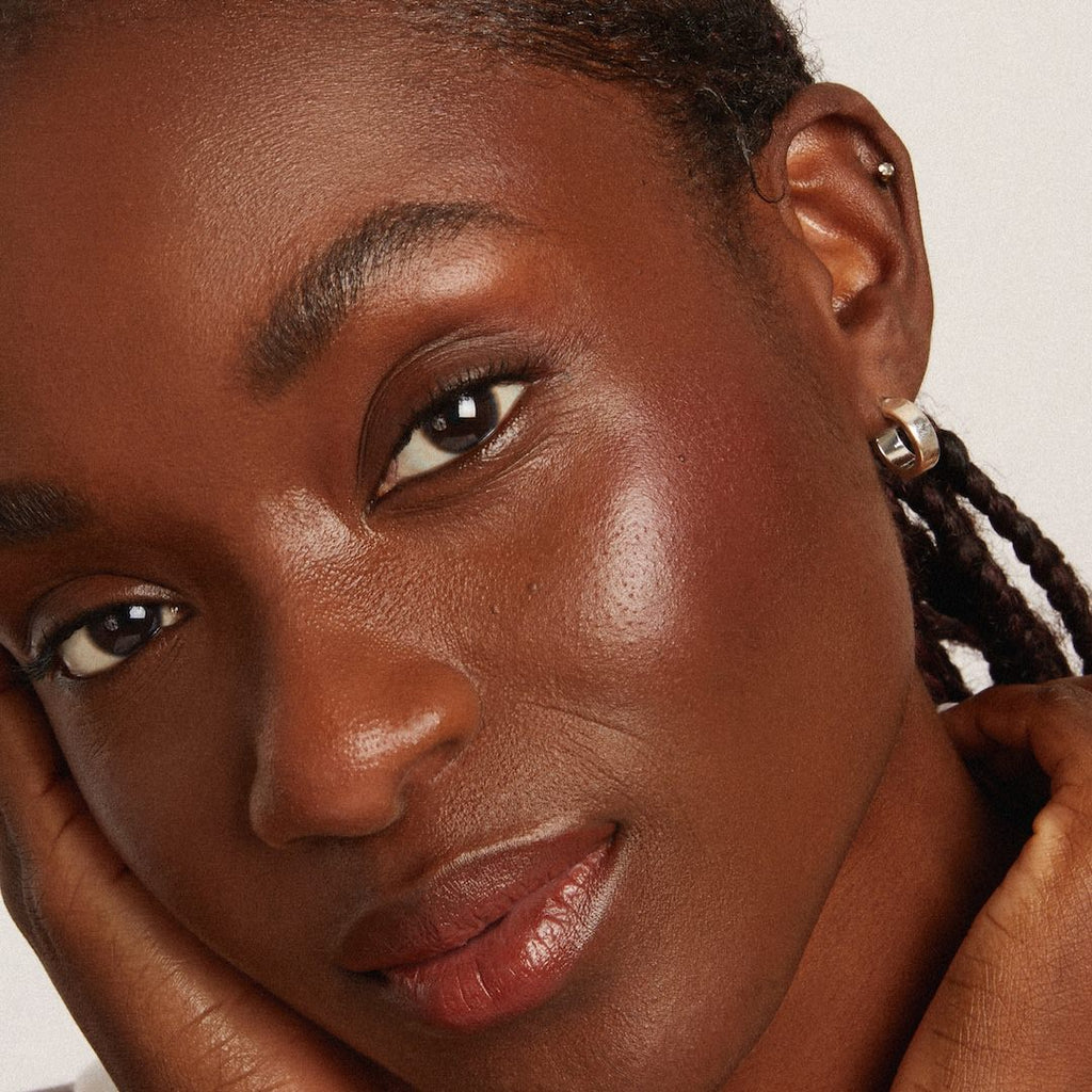 Close-up of a woman with braided hair wearing makeup against a neutral background