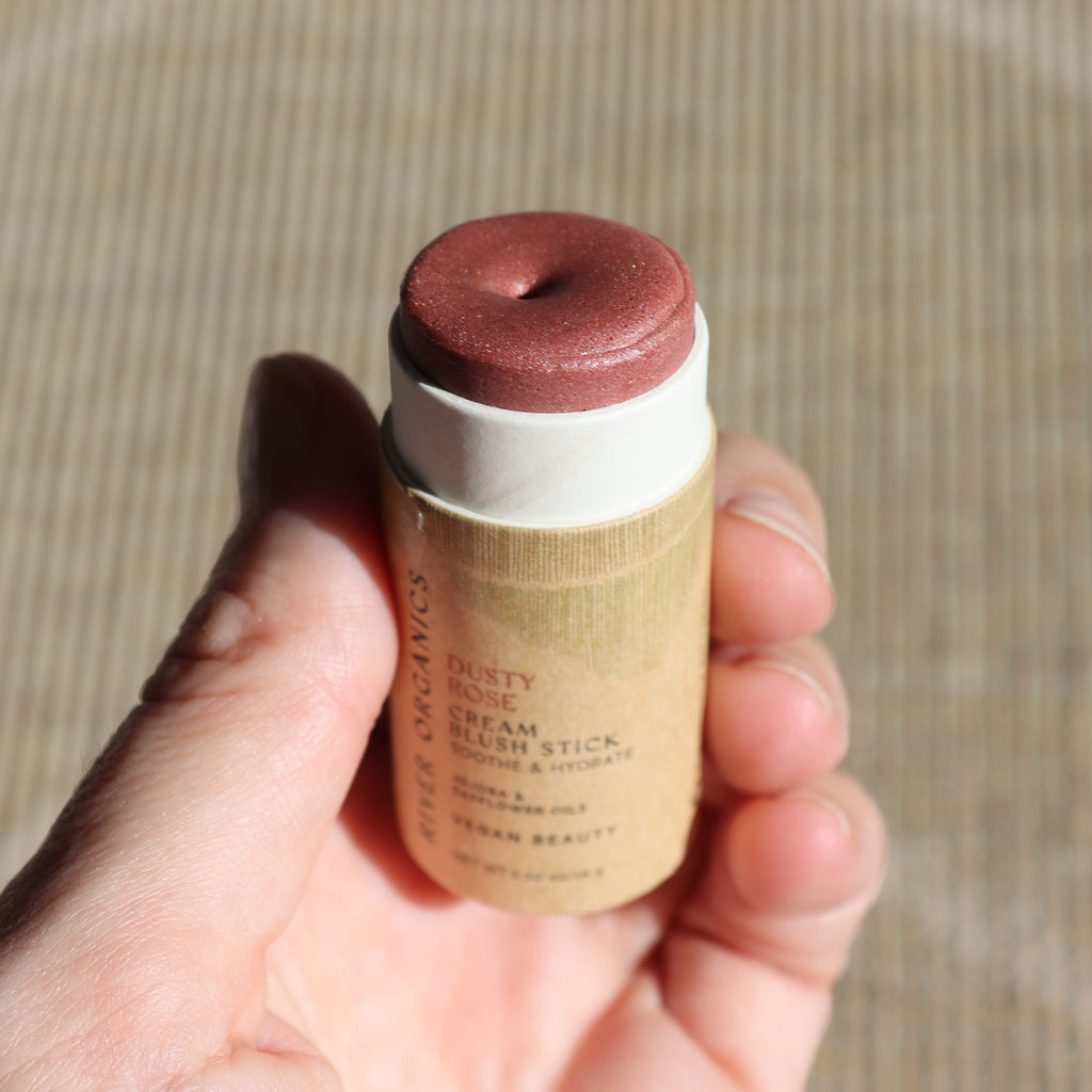 Hand holding a cream blush stick with a beige and brown color scheme.