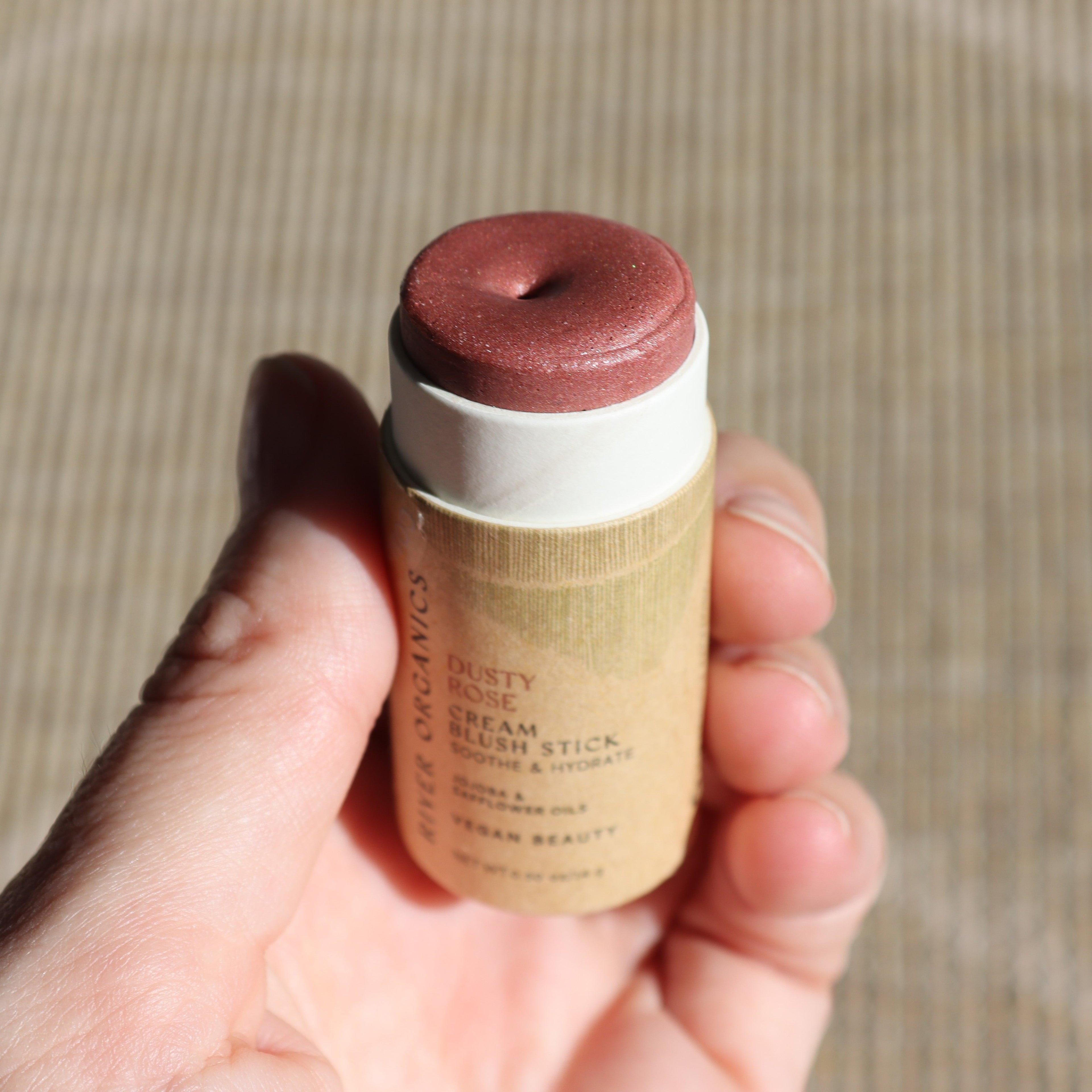 Hand holding a cream blush stick with a beige and brown color scheme.
