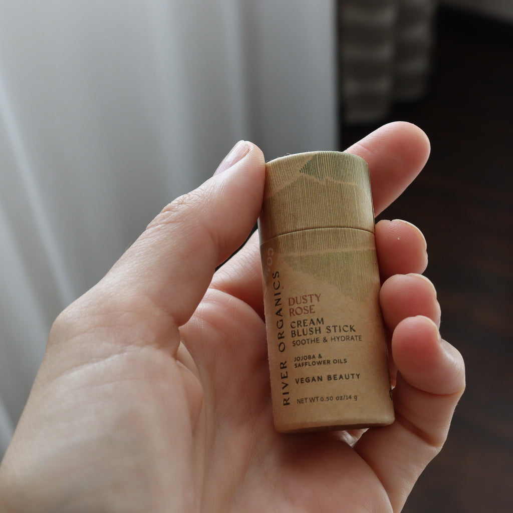 Hand holding a River Organics cream blush stick with a blurred background