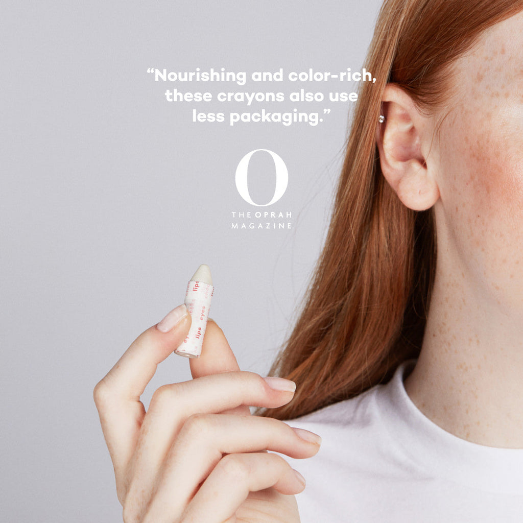 Person holding a crayon with text about nourishing makeup crayons and less packaging on a gray background.