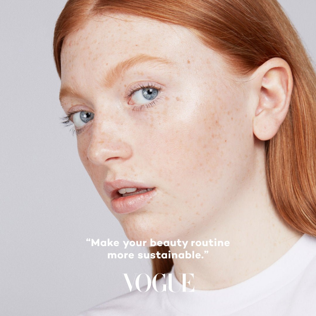 Close-up of a person with red hair wearing makeup, with a Vogue logo and text about sustainability.
