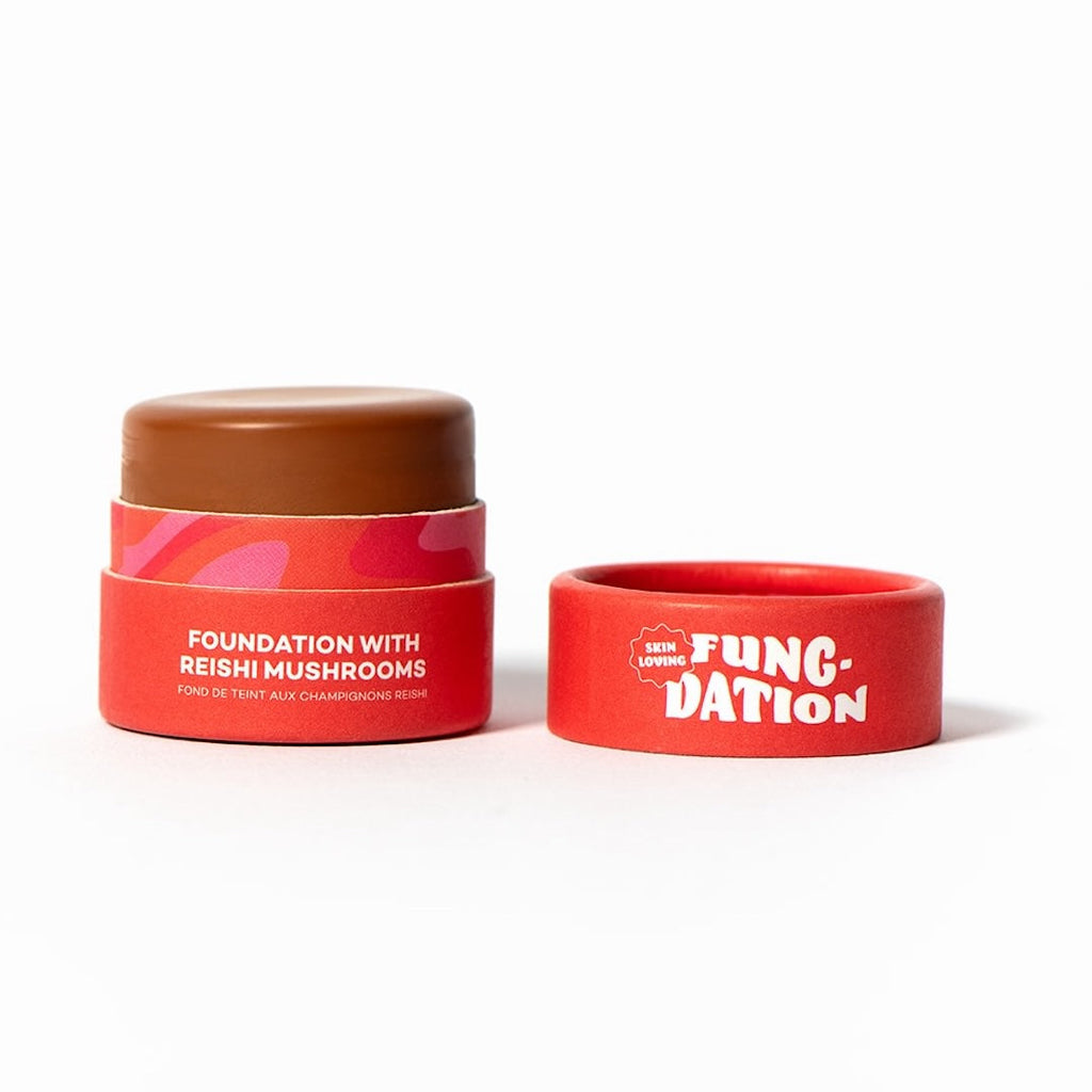 Red cosmetic pot with brown foundation and red lid on a white background