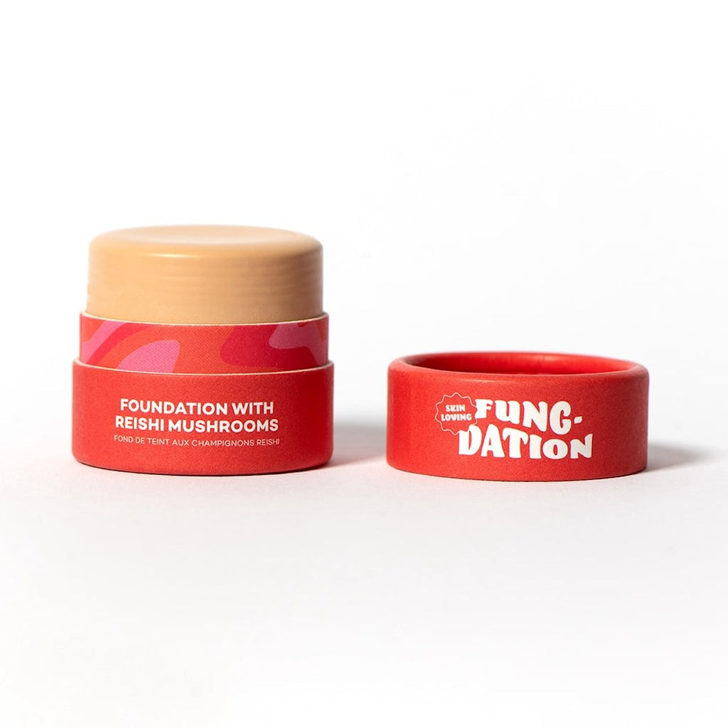 Red cosmetic pot with beige foundation and a red lid on a white background