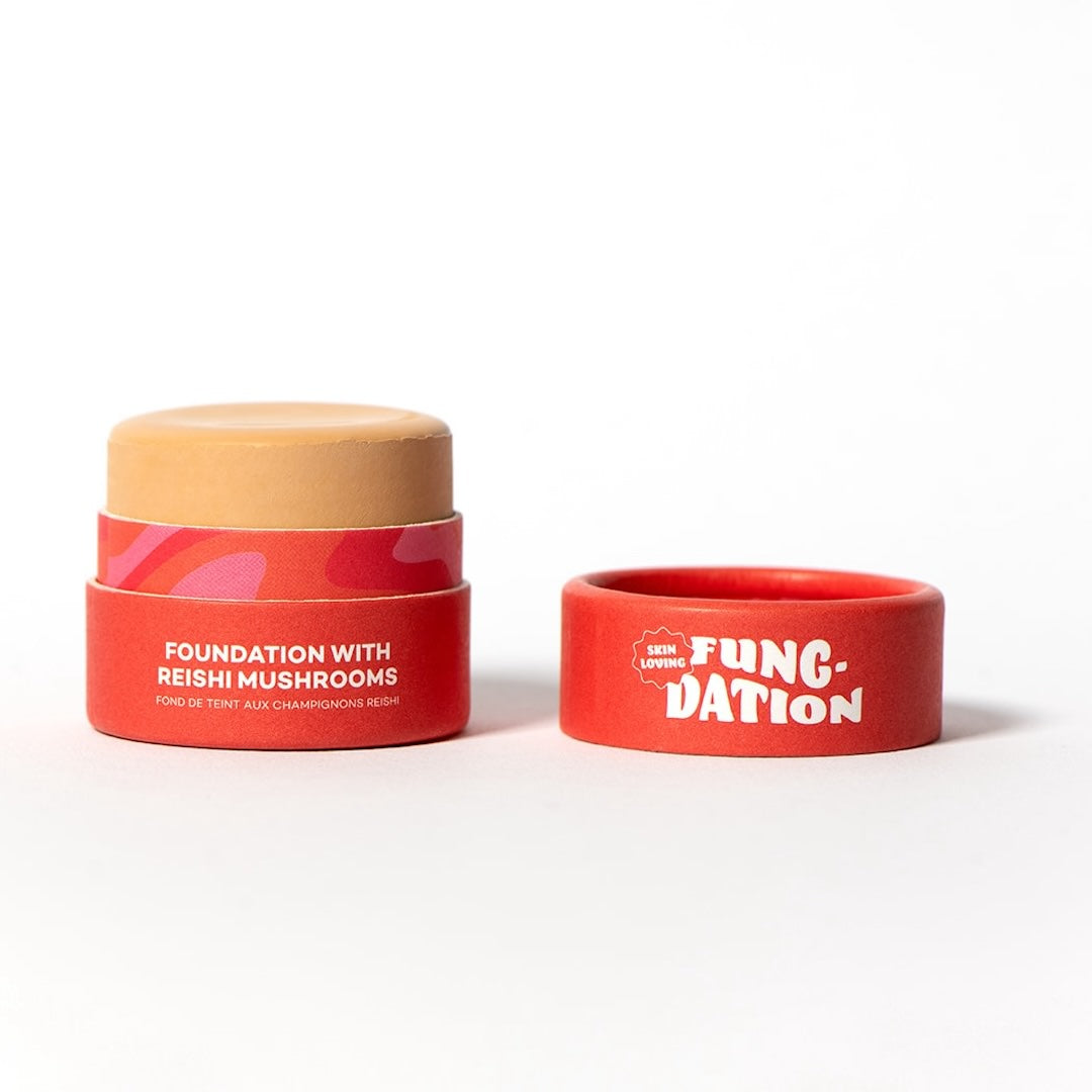 Red cosmetic pot with beige foundation and red lid on a white background