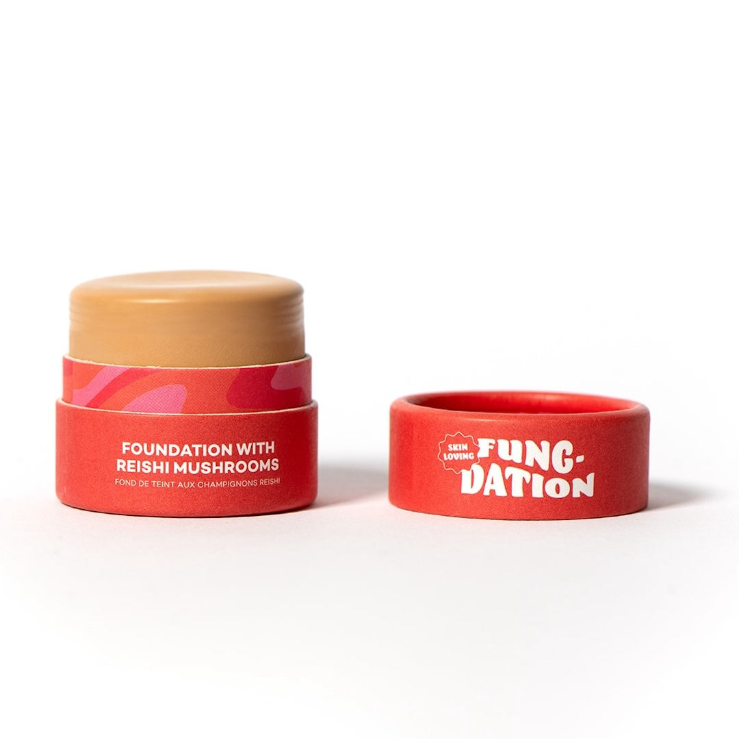 Red cosmetic pot with beige foundation and red lid on a white background