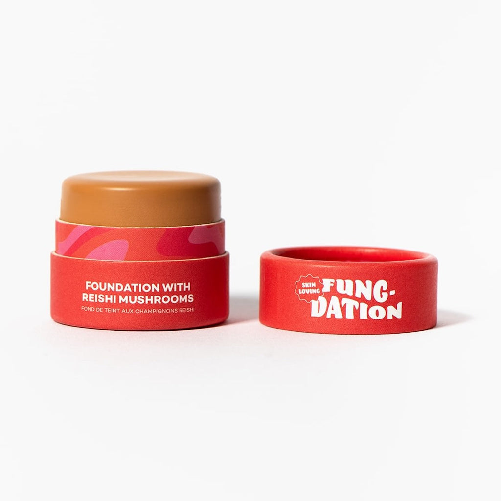 Red cosmetic pot with light brown foundation and red lid on a white background