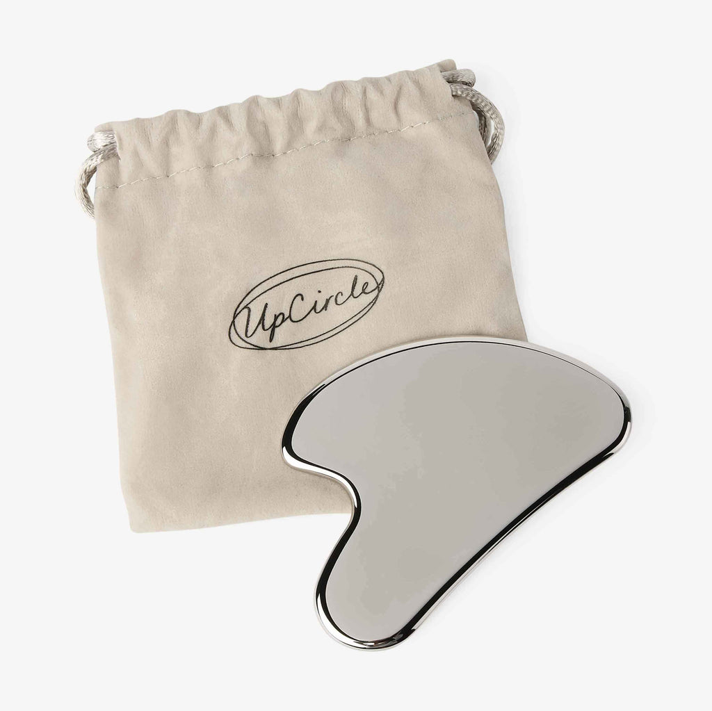 Silver and beige gua sha tool with a beige drawstring bag featuring 'UpCircle' branding on a white background.