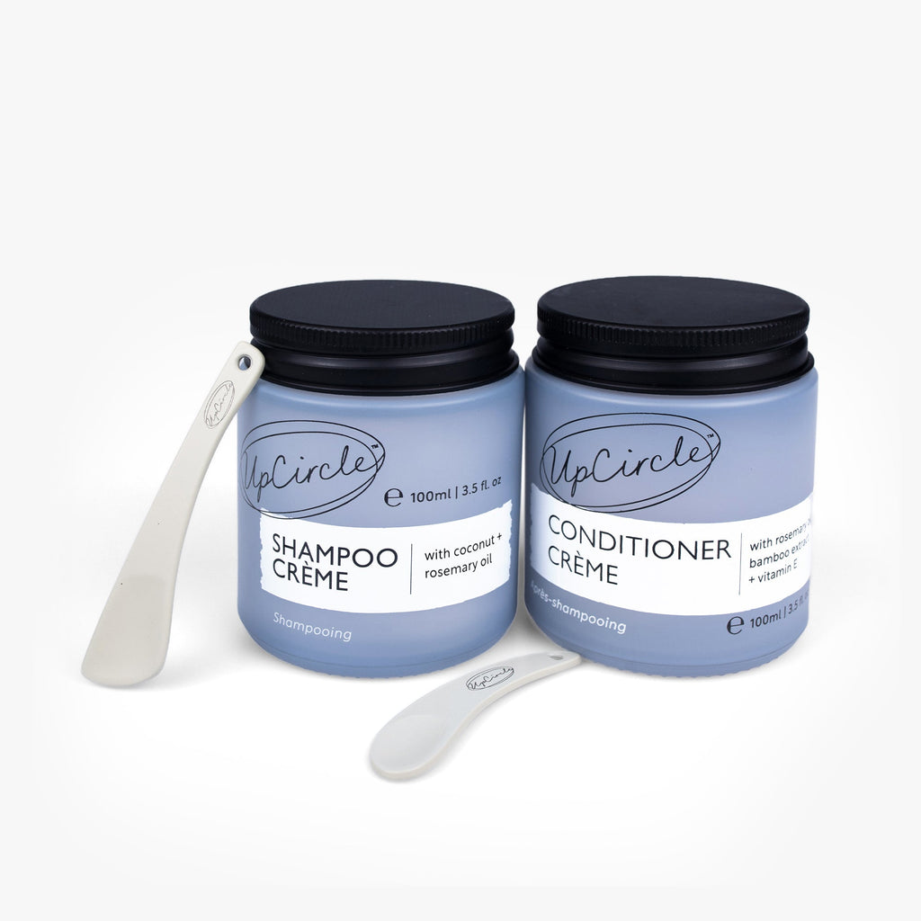 Two jars of UpCircle Shampoo Crème and Conditioner Crème with black lids on a white background.