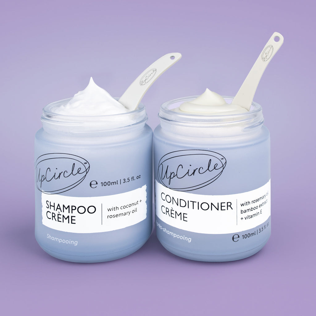 Two jars of UpCircle Shampoo Crème and Conditioner Crème on a purple background