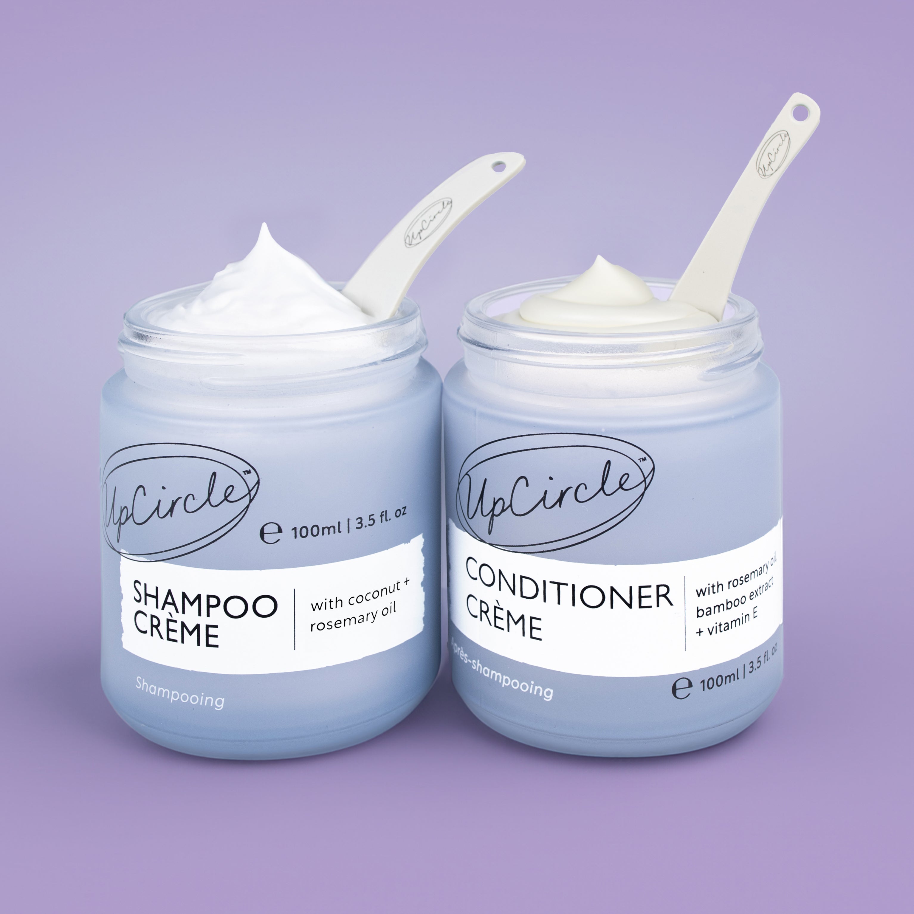Two jars of UpCircle Shampoo Crème and Conditioner Crème on a purple background