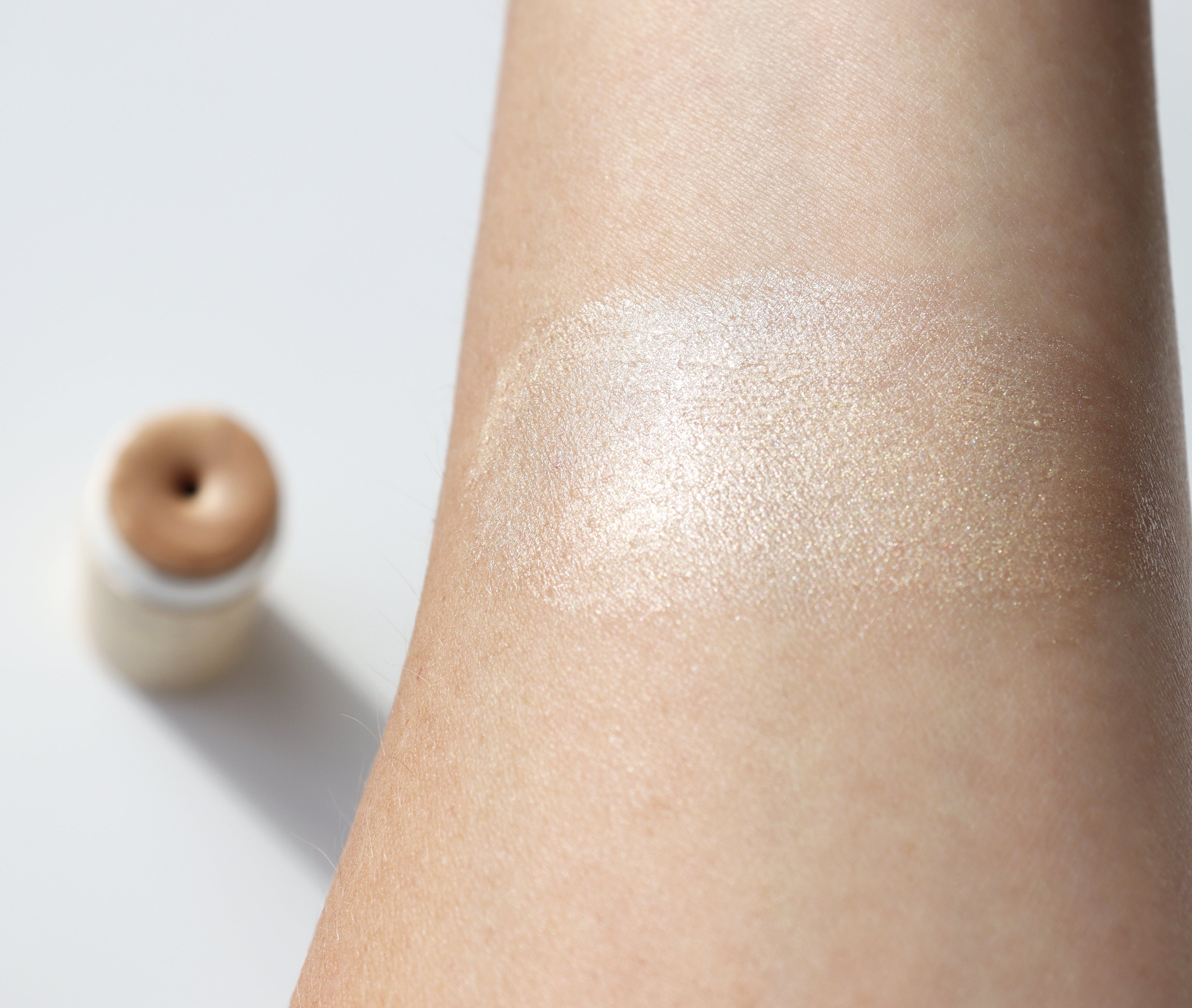 Close-up of a person's arm with a shimmery makeup product applied, with a highlighter stick in the background.