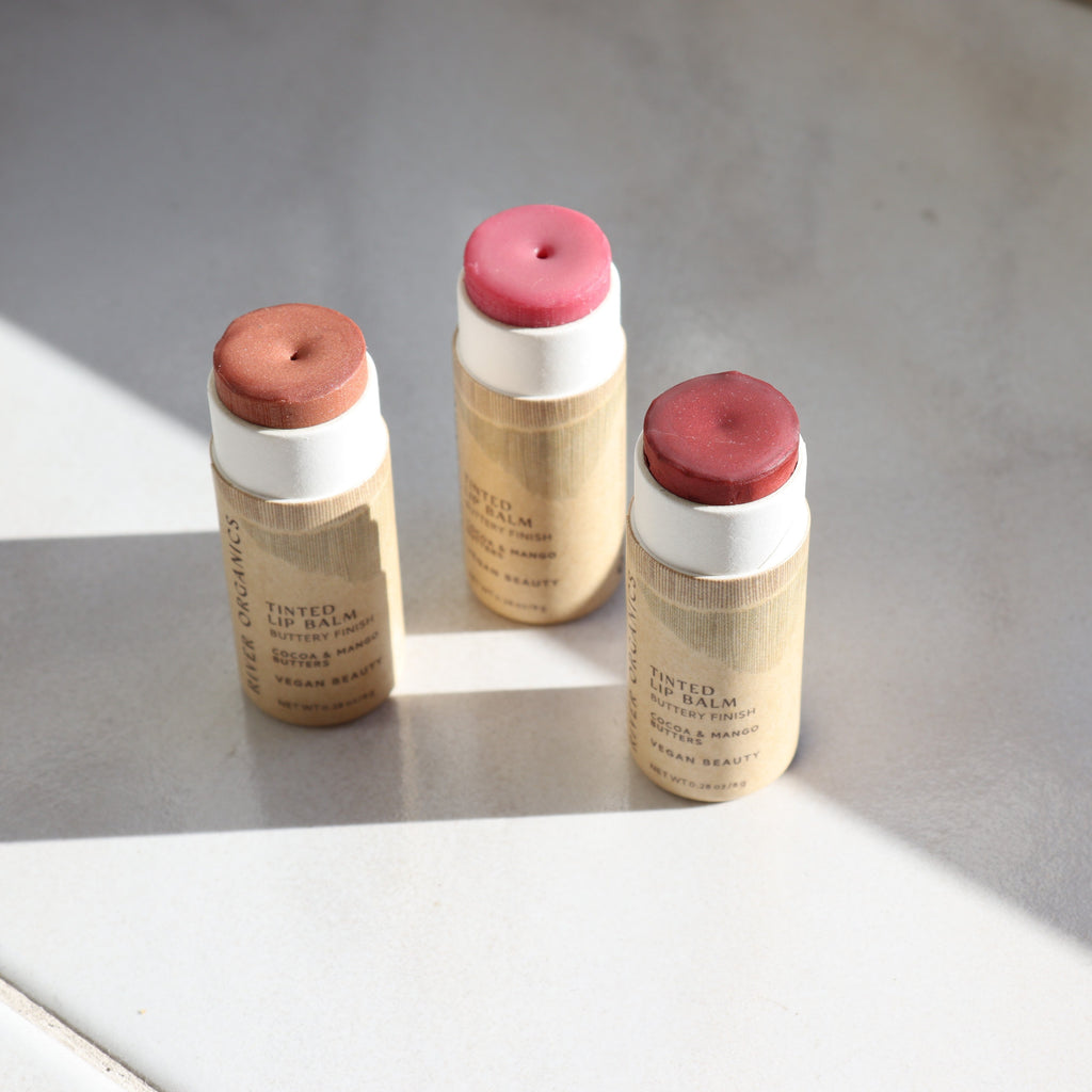 Three tinted lip balm tubes with paper packaging on a light gray surface