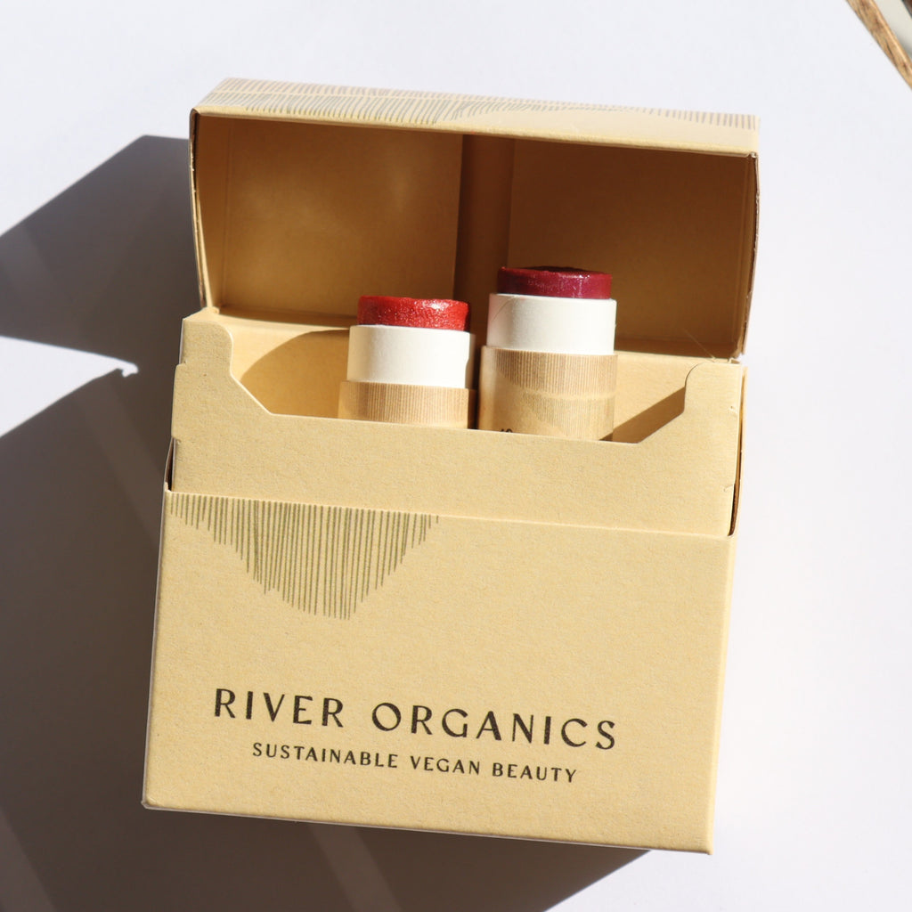 Open cardboard box containing two cosmetic tubes, branded 'River Organics'.