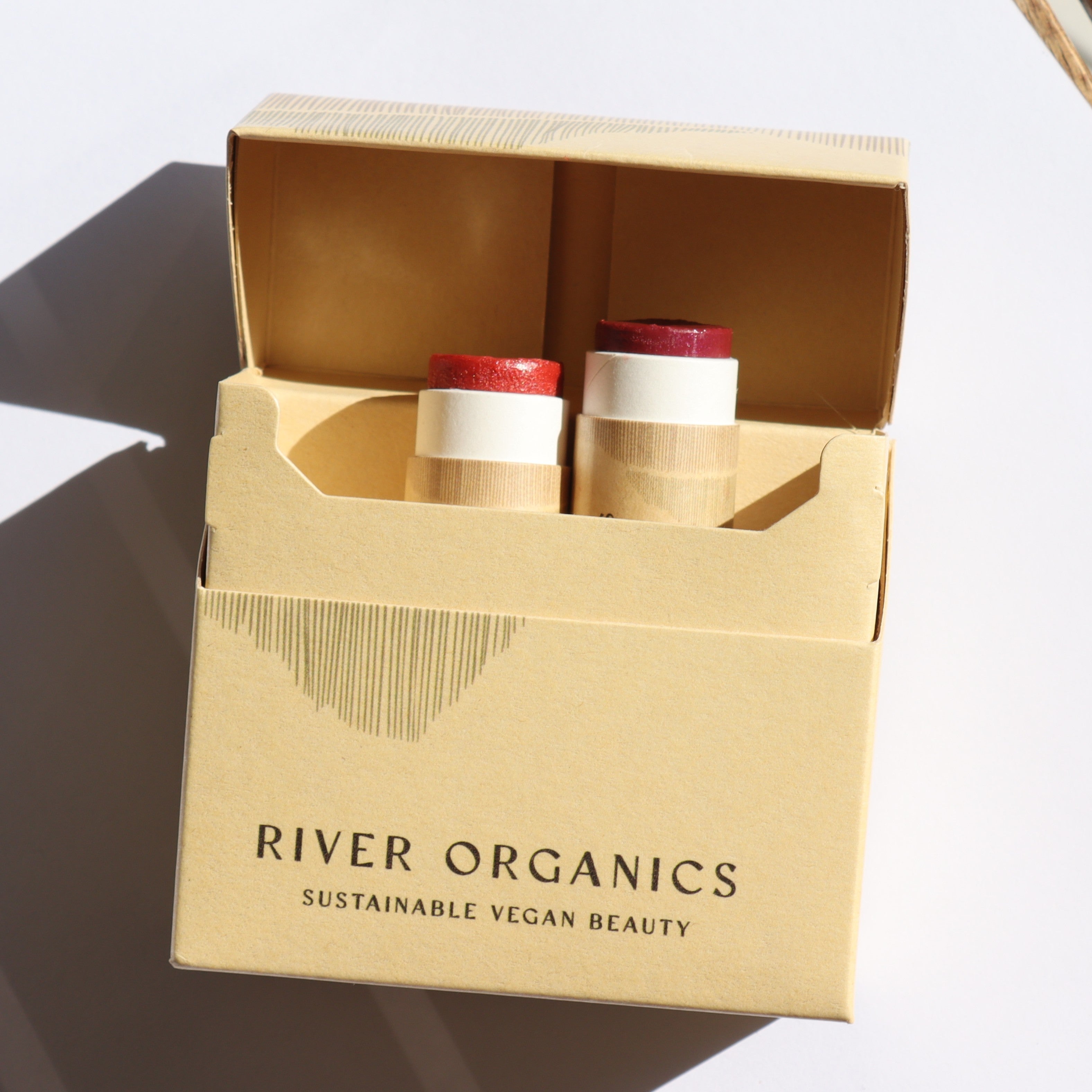 Open cardboard box containing two cosmetic tubes, branded 'River Organics'.