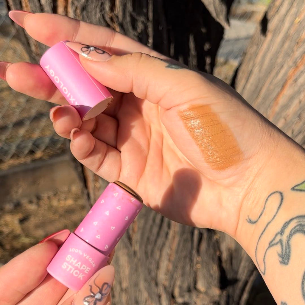 Hand holding a pink makeup tube with a swatch on the palm against a natural background