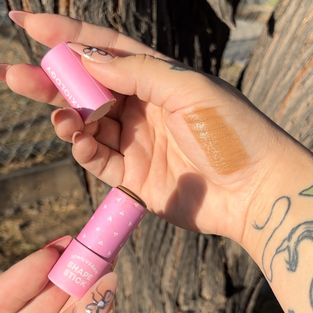 Hand holding a pink makeup tube with a swatch on the palm against a natural background