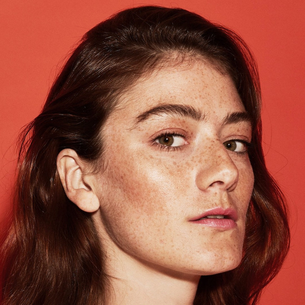 Close-up of a person with freckles wearing makeup against a red background