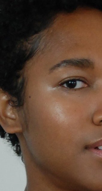 Close-up of a person's face with a neutral expression wearing neutral makeup on a plain background