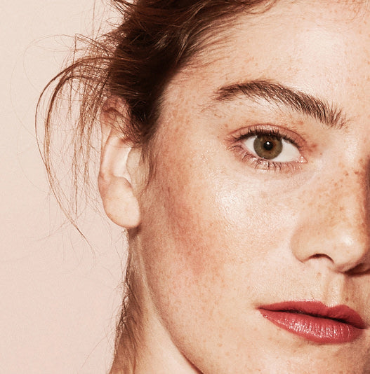 Close-up of a woman's face wearing makeup with a soft pink background