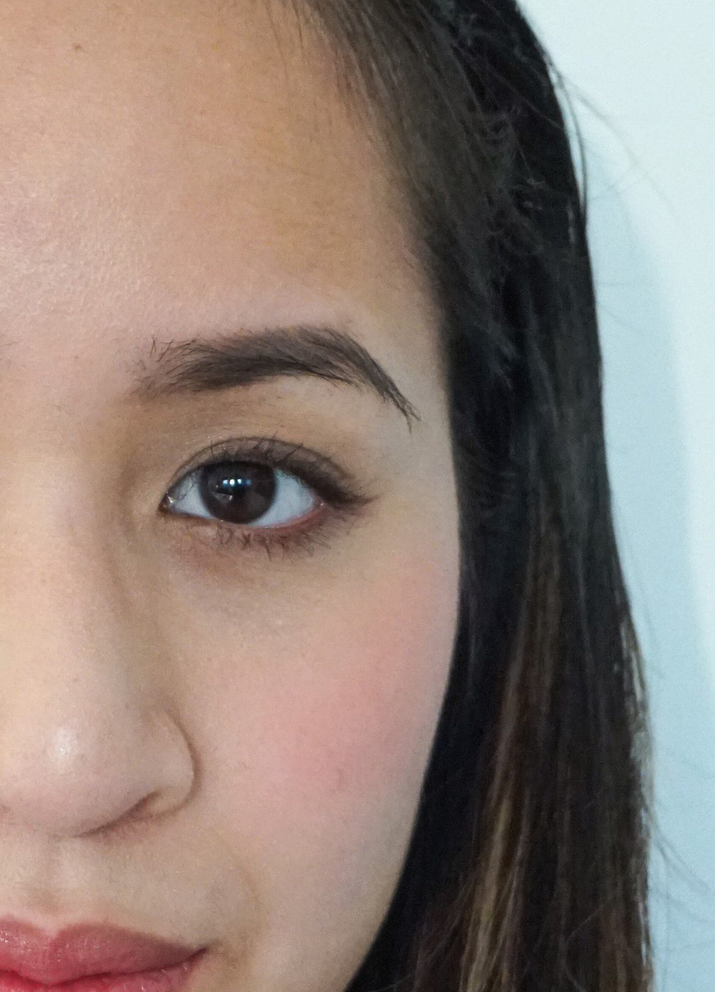 Close-up of a person's face with a neutral expression wearing makeup on a plain background