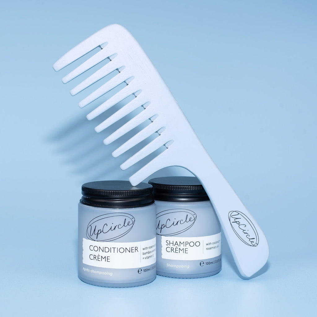 Two jars of UpCircle hair care products with a comb on a light blue background