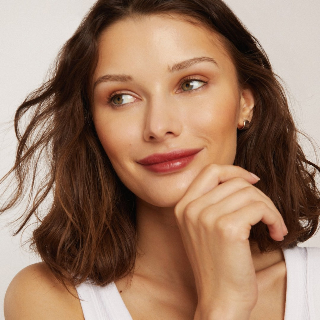 Woman with wavy brown hair and red lipstick posing against a plain background