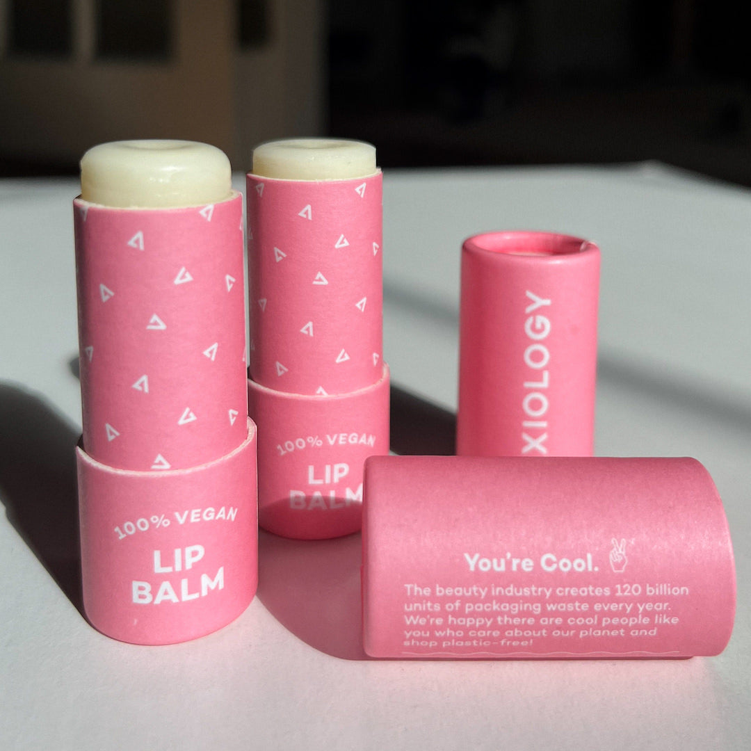 Pink lip balm containers with 'AXIOLOGY' branding on a light surface.