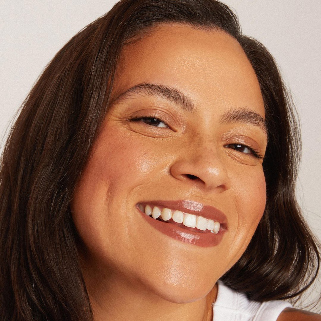Close-up of a woman with a warm smile wearing foundation makeup against a neutral background