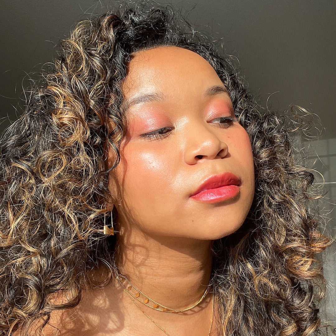 Woman with curly hair and pink makeup against a neutral background