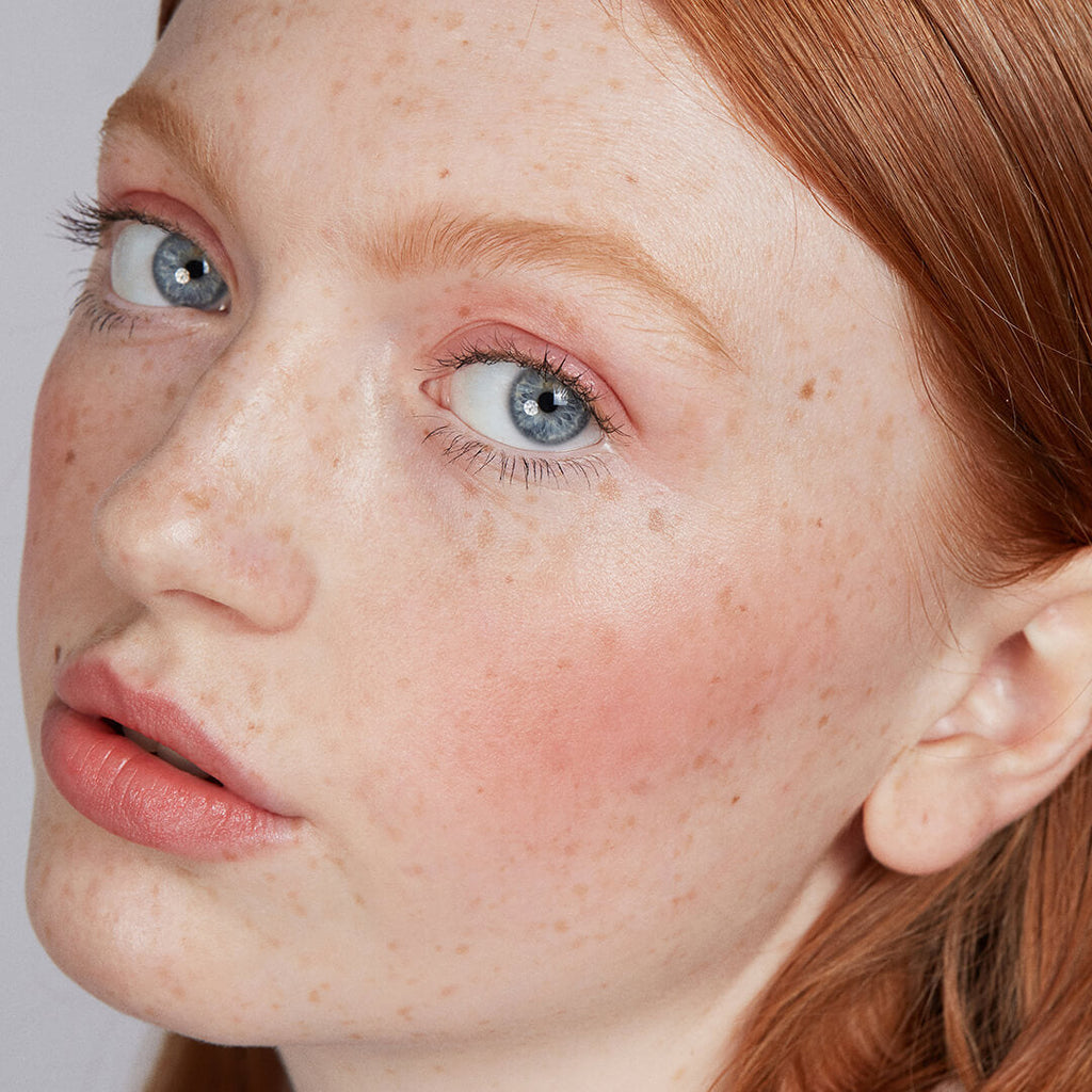 Close-up of a person with makeup and red hair and blue eyes on a plain background