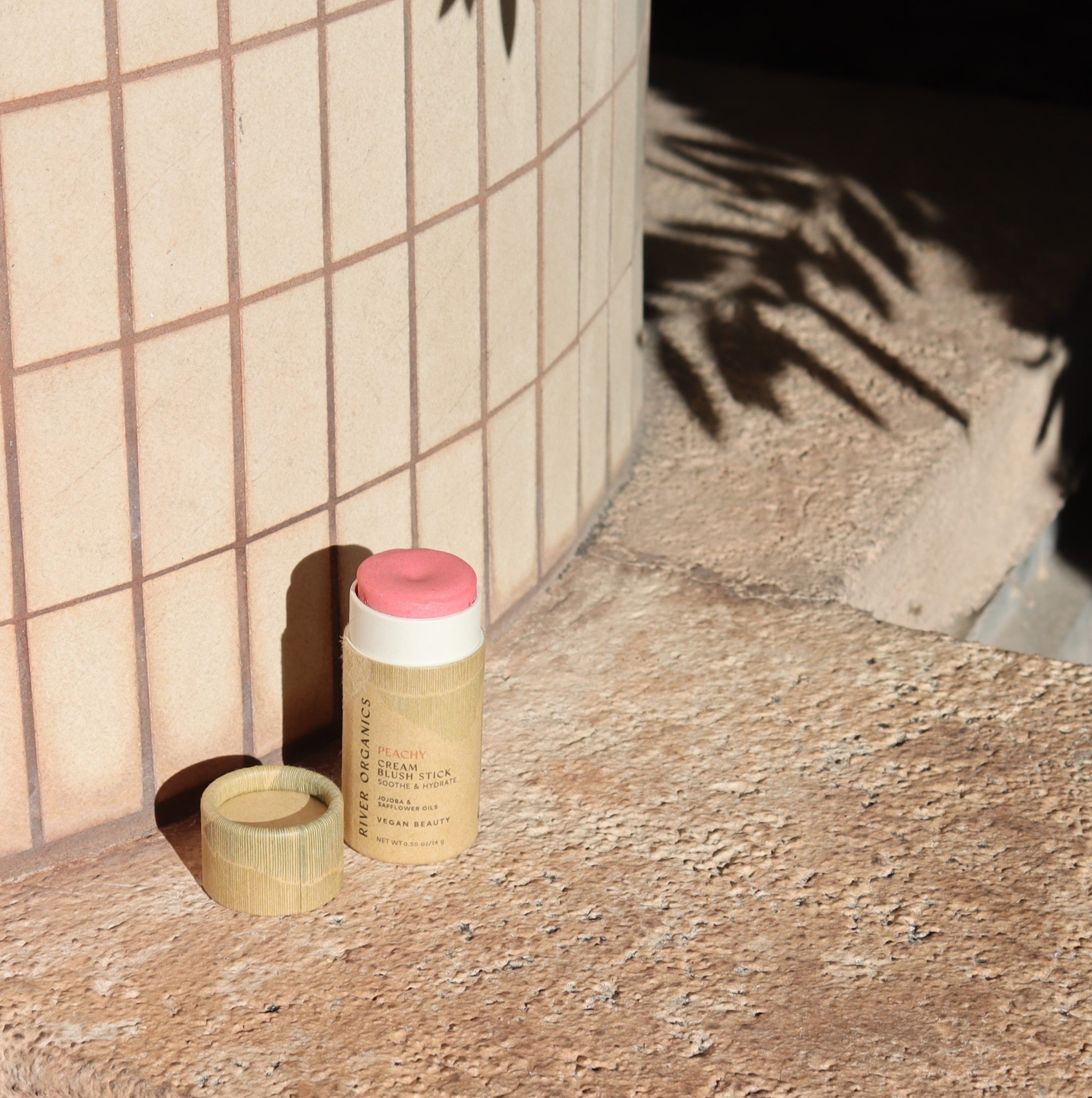 Blush stick with paper cap on a textured surface next to a tiled wall
