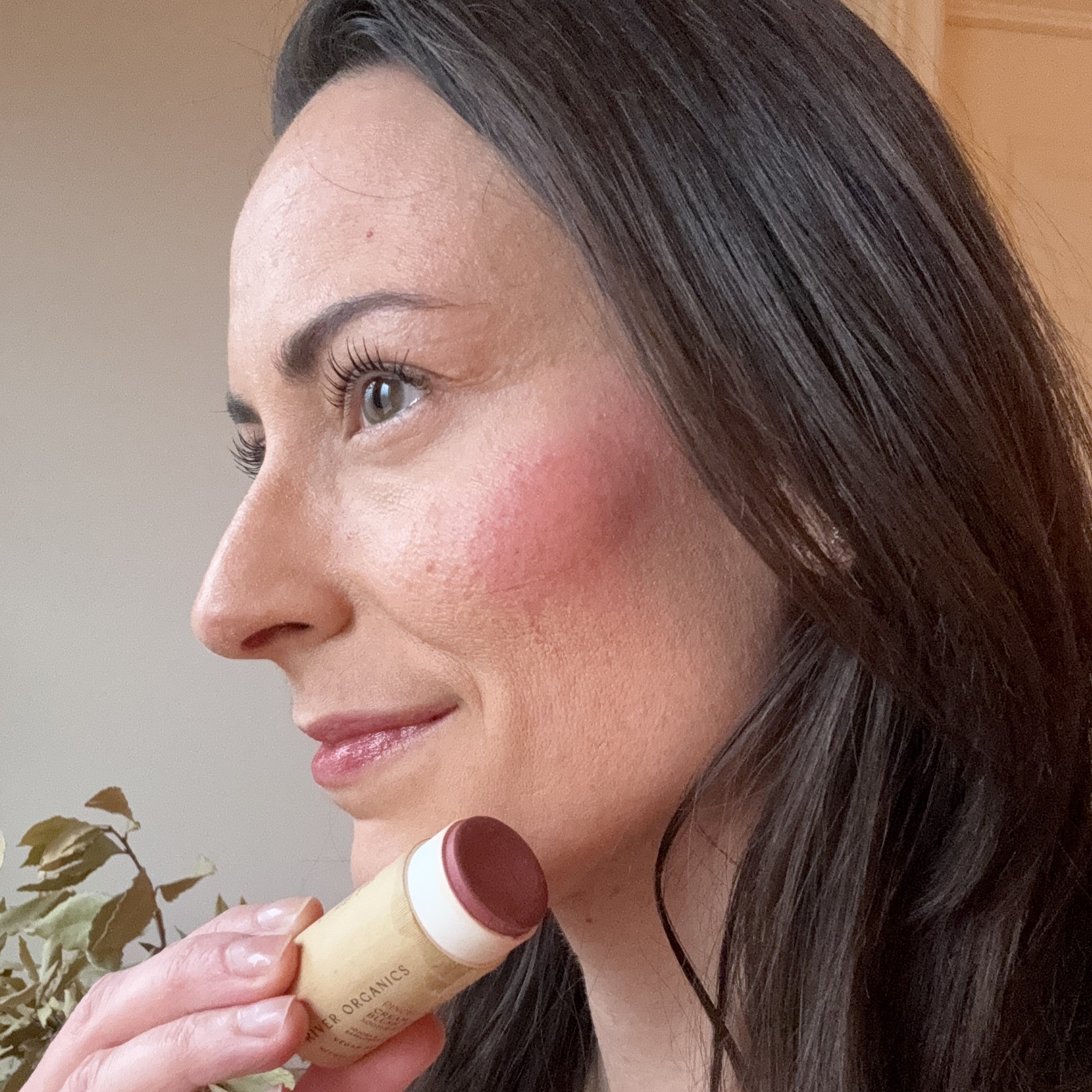 Woman applying makeup with a blush stick near her face