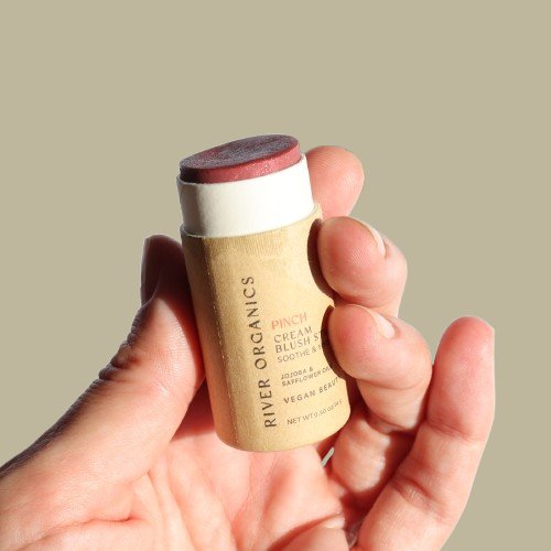 Hand holding a River Organics blush stick against a beige background