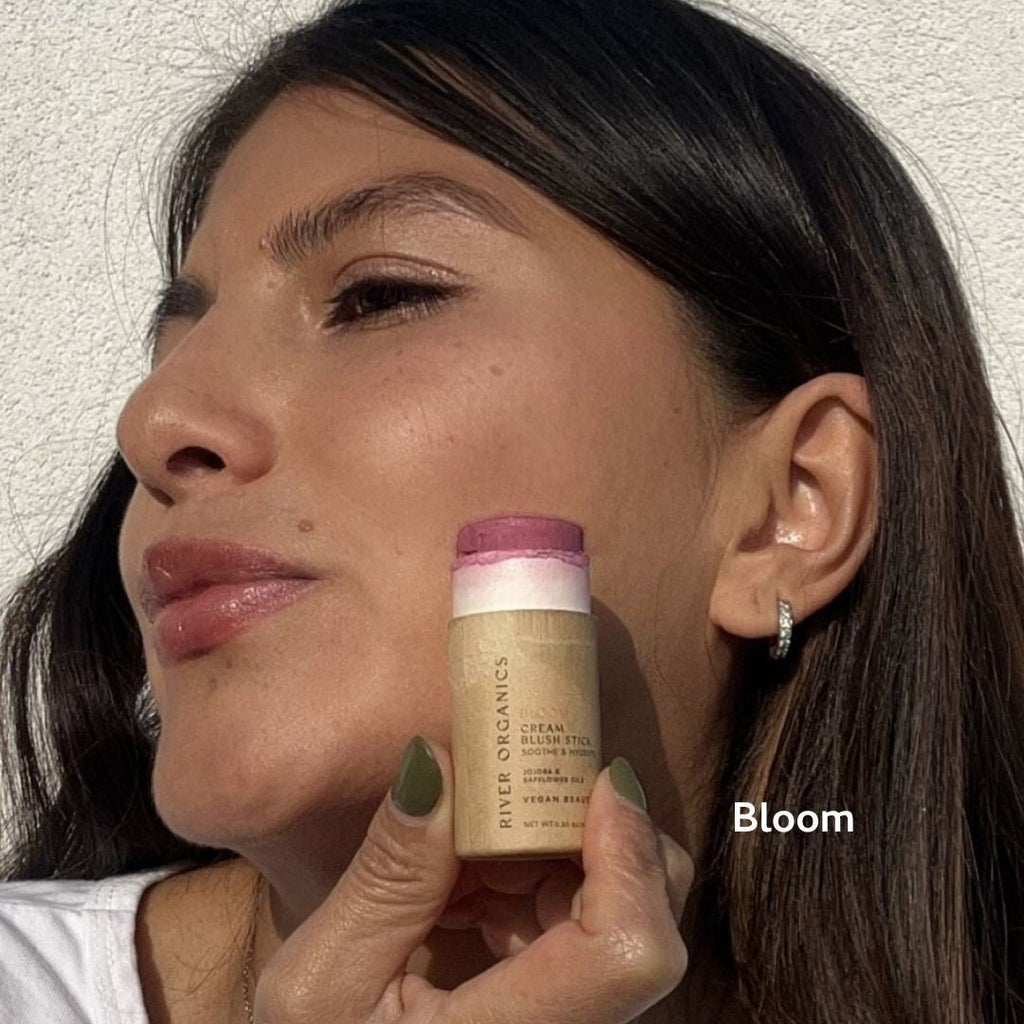 Woman holding a blush stick labeled 'Bloom' against a neutral background