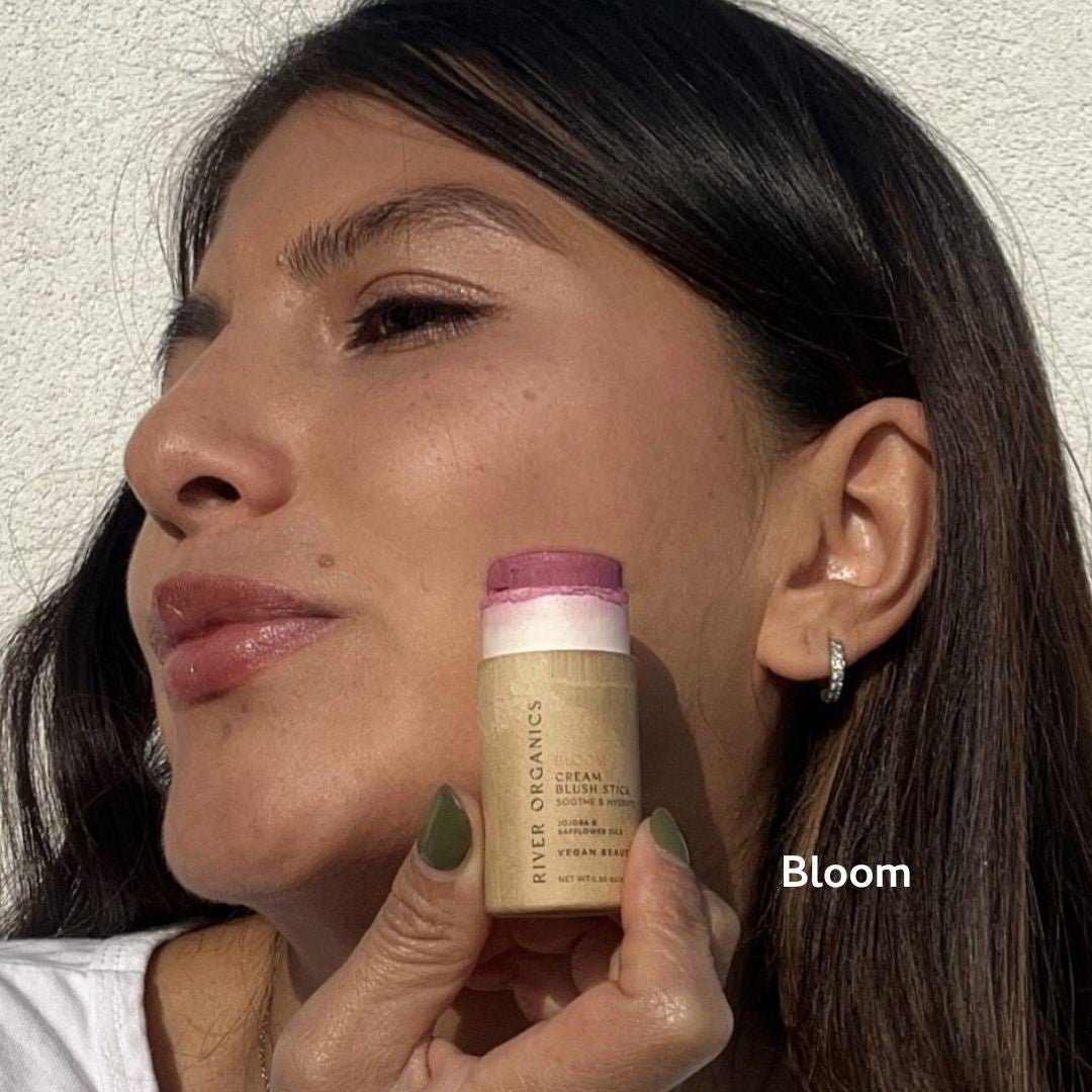 Woman holding a blush stick labeled 'Bloom' against a neutral background
