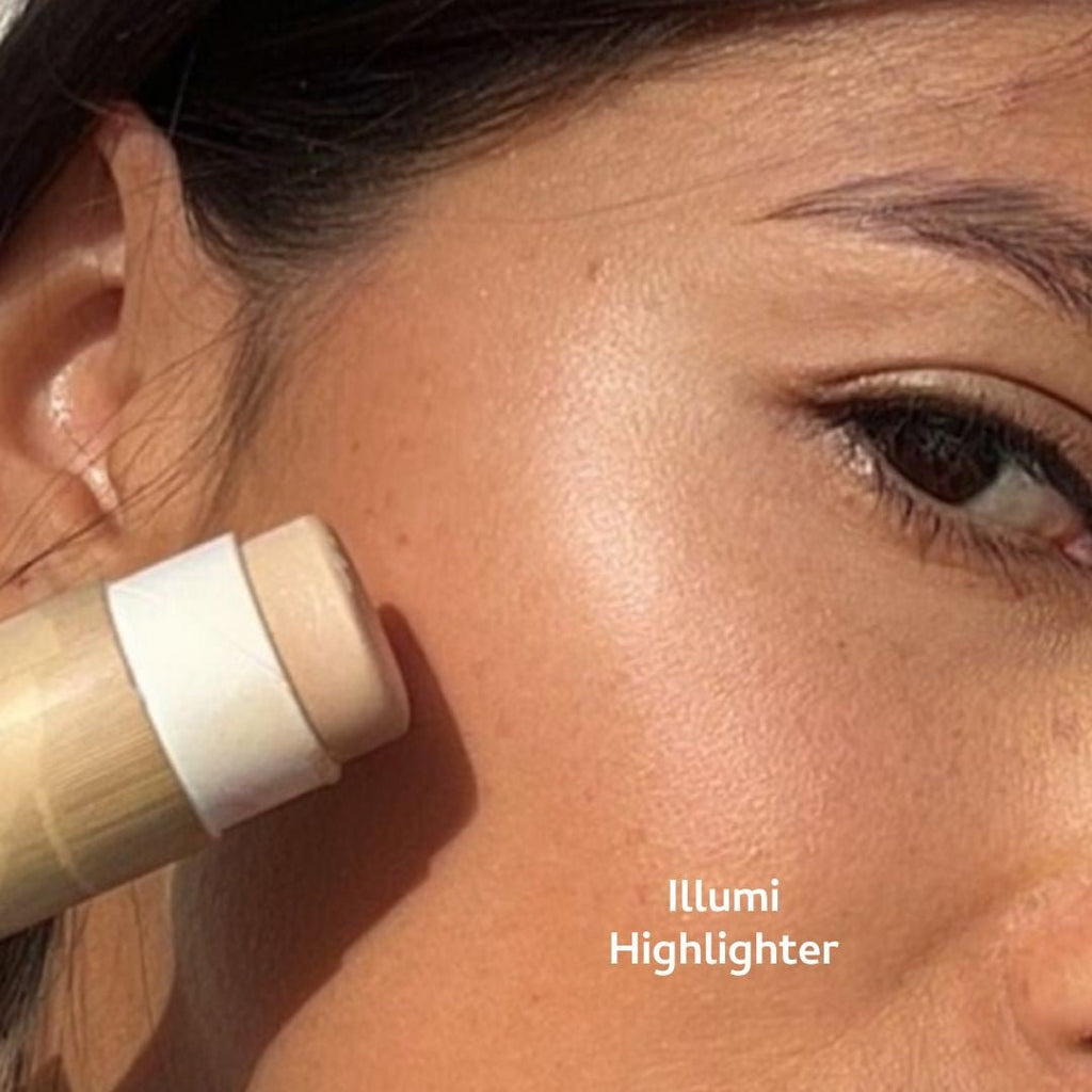 Woman applying highlighter stick to her face, product labeled 'Illumi Highlighter'.
