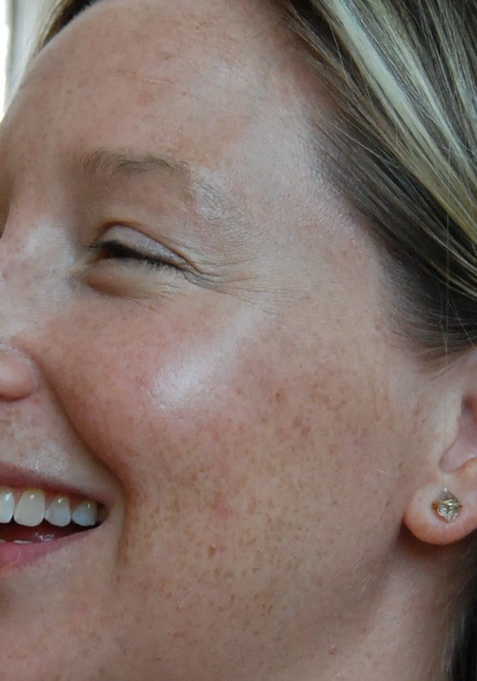 Close-up of a person's face with visible freckles wearing highlighter makeup.