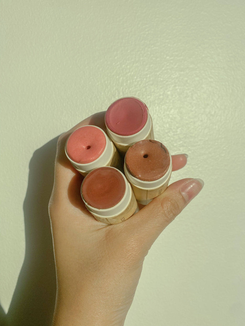 Hand holding four blush sticks against a light background