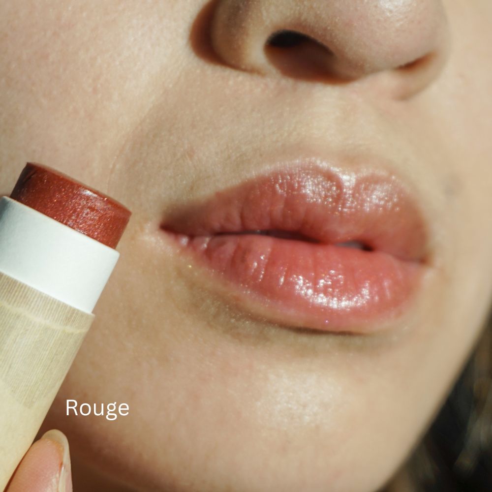 Close-up of a person applying tinted lip balm labeled 'Rouge' with a blurred background.