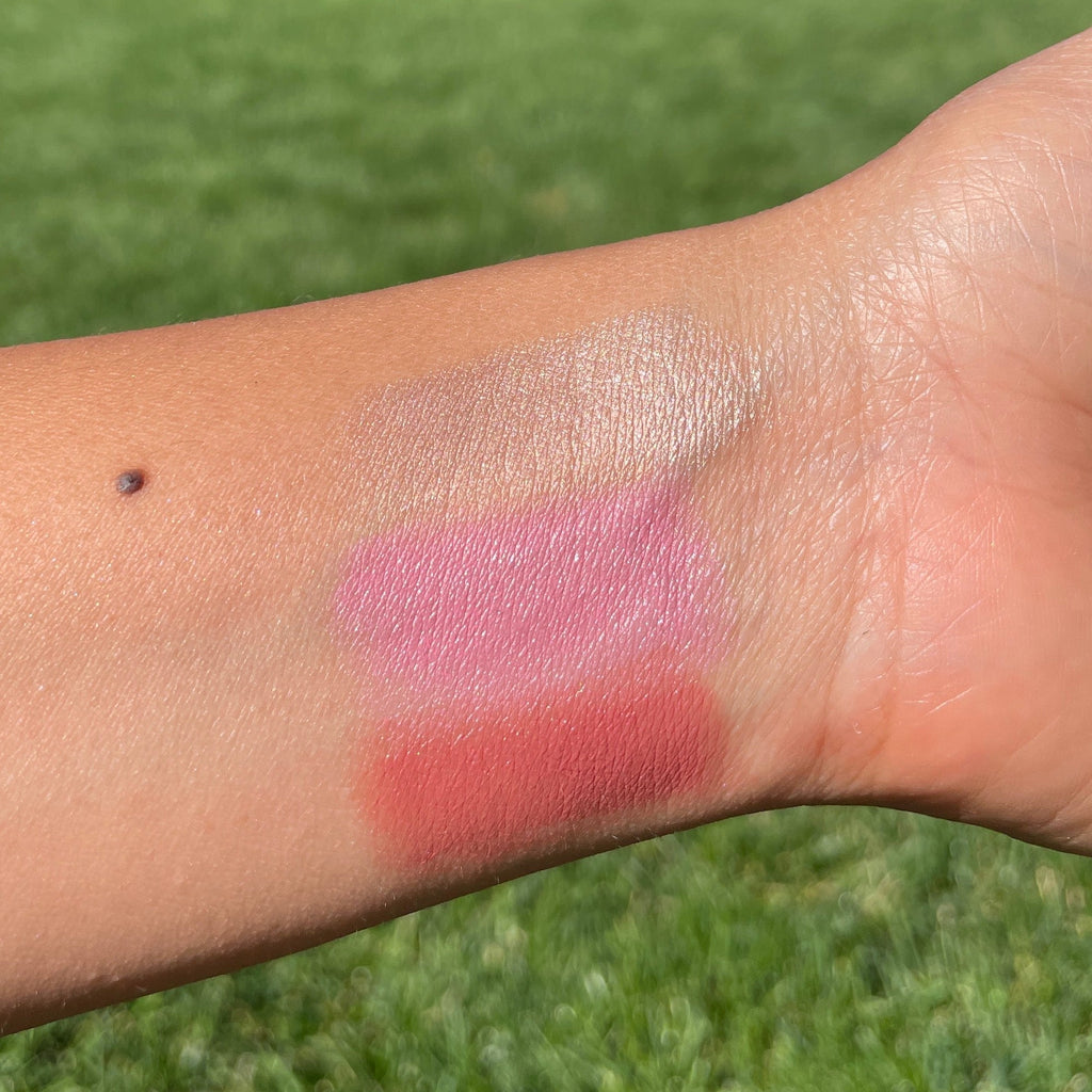 Swatches of pink and red makeup on a person's arm with a grassy background