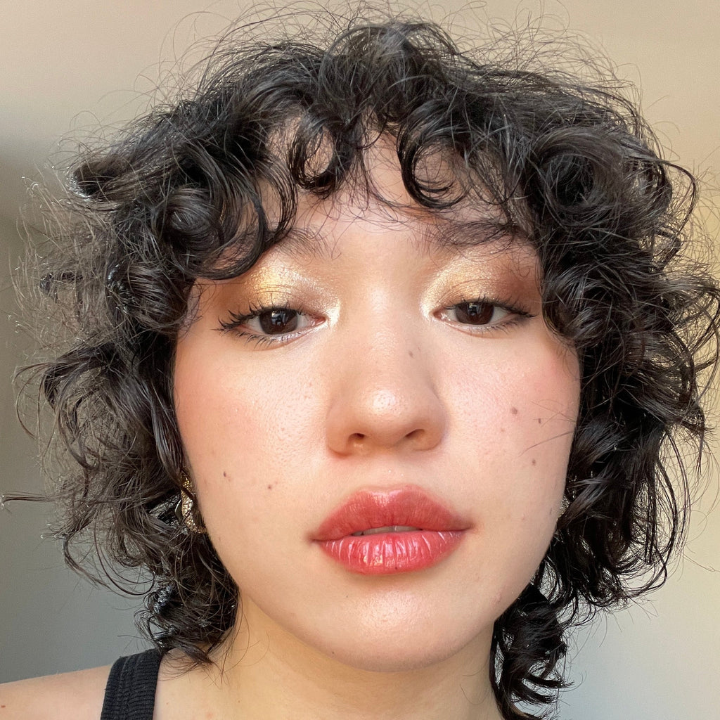 Close-up of a person with curly hair and red lipstick against a neutral background