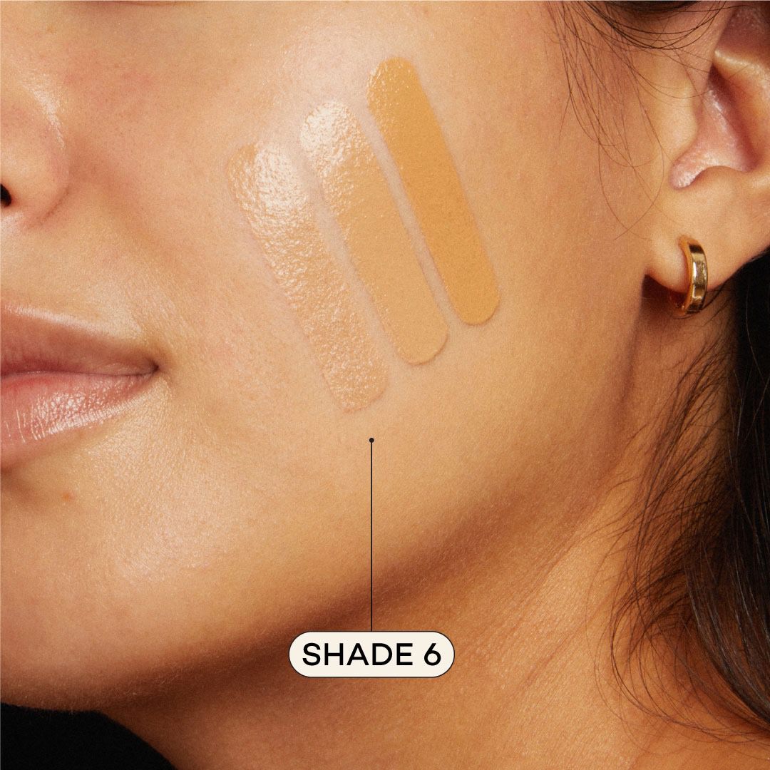 Close-up of a woman's face with foundation swatches on her cheek, labeled 'Shade 6'.