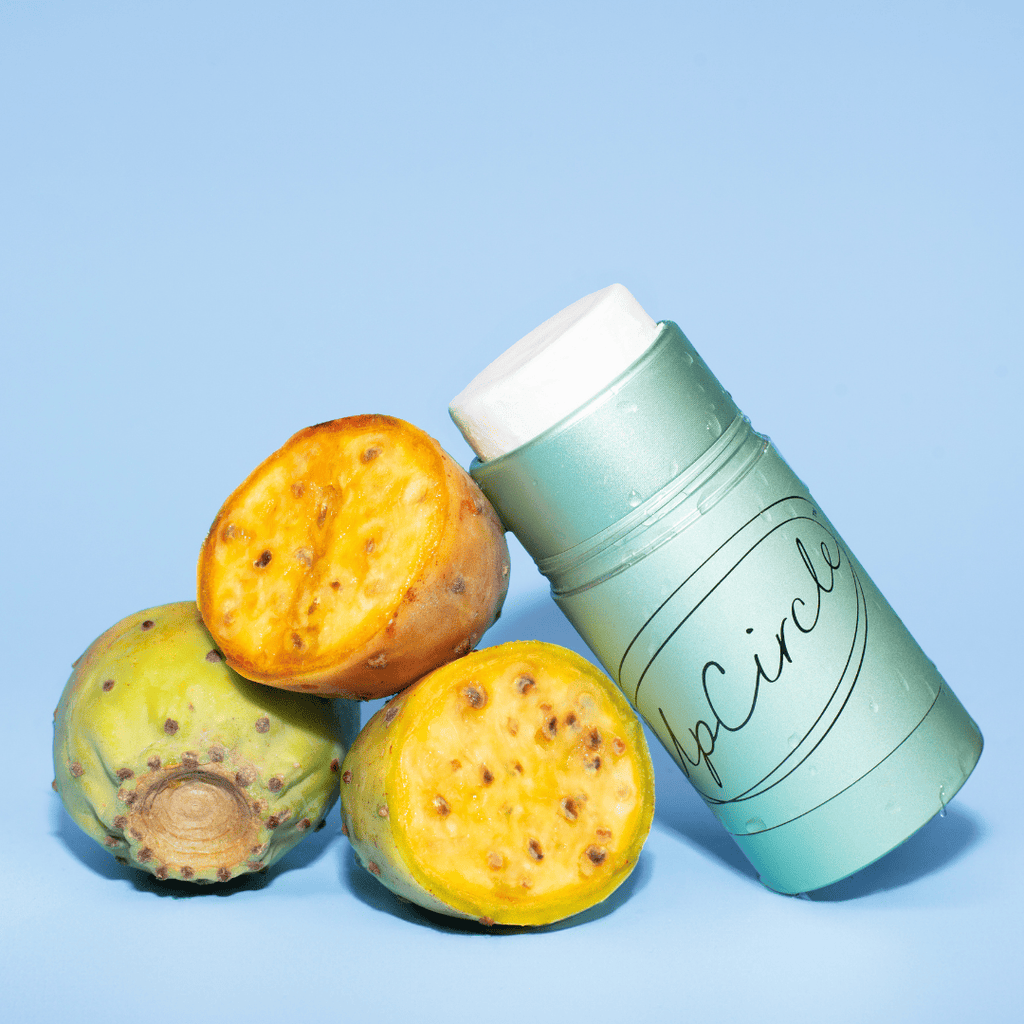 Green cylindrical deodorant container labeled 'UpCircle' next to prickly pear cactus fruits on a light blue background