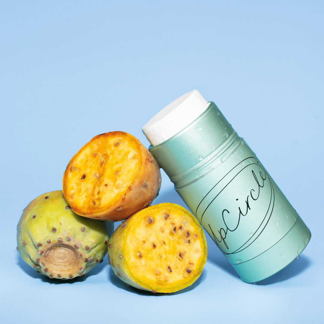 Green cylindrical deodorant container labeled 'UpCircle' next to prickly pear cactus fruits on a light blue background