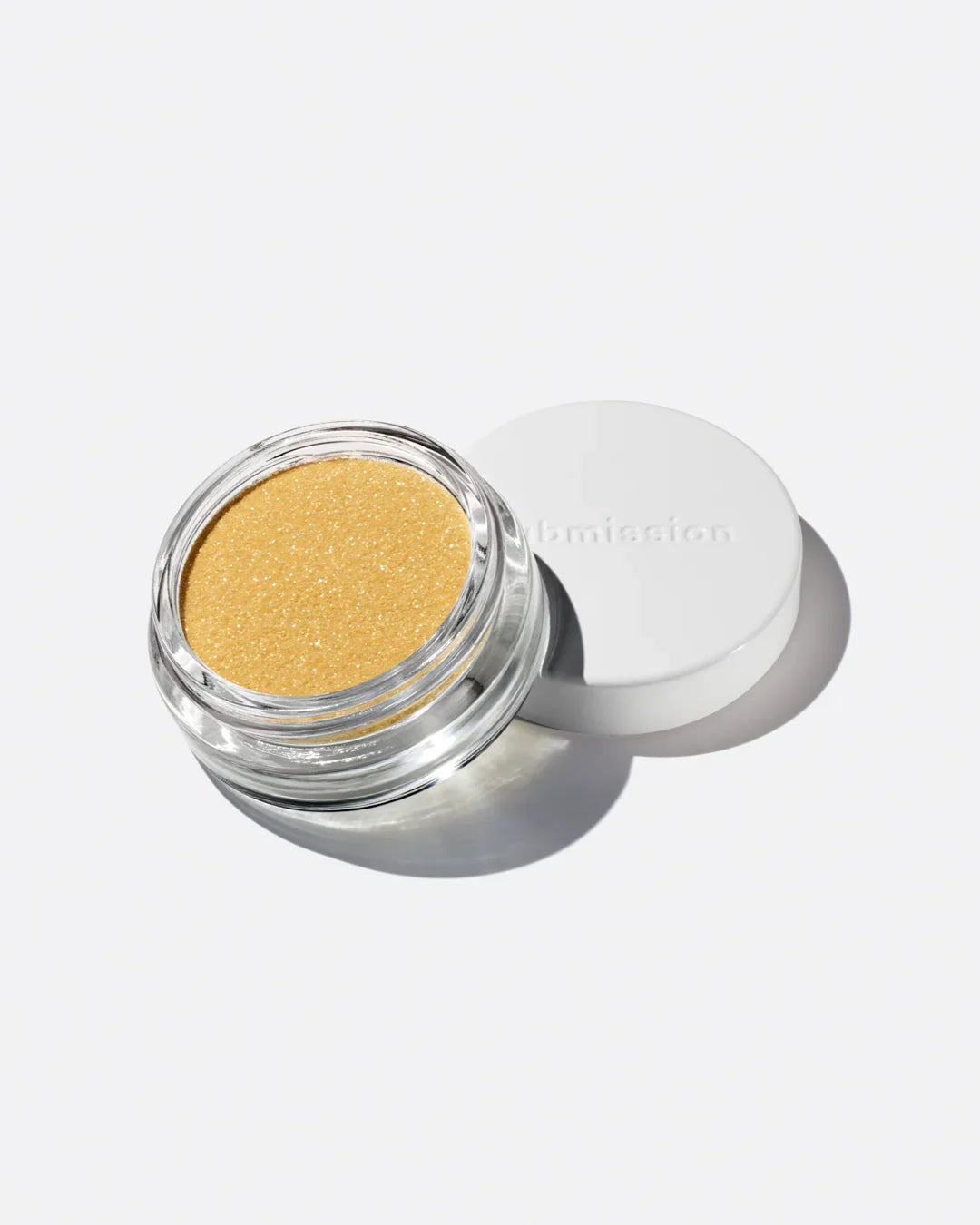 Gold glitter eyeshadow in a open jar with a white lid on a light gray background