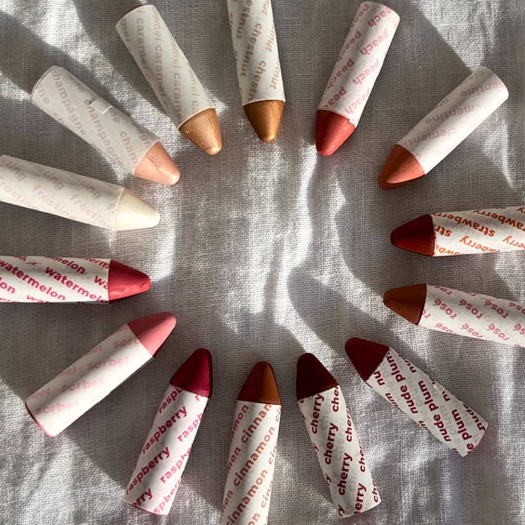 Assorted lip crayons arranged in a circular pattern on a textured surface.