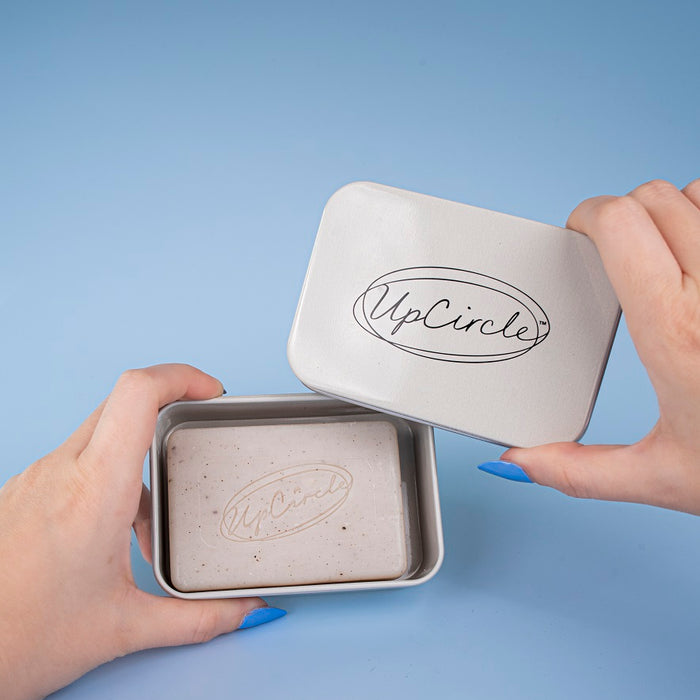 Person holding a metallic tin with 'UpCircle' branding against a blue background